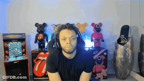 A Man Wearing Headphones Sits In Front Of A Pac Man Machine GIF