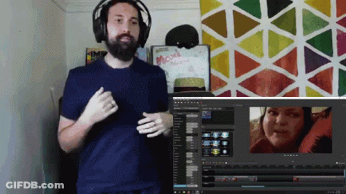 A Man Wearing Headphones Stands In Front Of A Computer Screen With A Sign That Says Maxi On It GIF