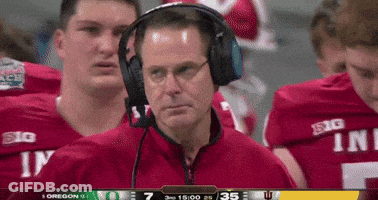 A Man Wearing Headphones Stands In Front Of A Group Of Football Players Wearing Red Jerseys That Say Big GIF