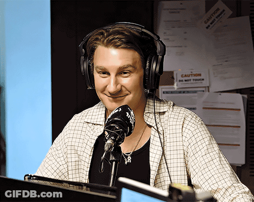 A Man Wearing Headphones Stands In Front Of A Microphone GIF