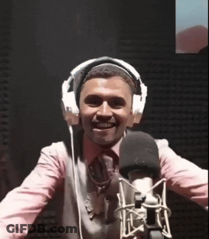 A Man Wearing Headphones Stands In Front Of A Microphone And Smiles GIF