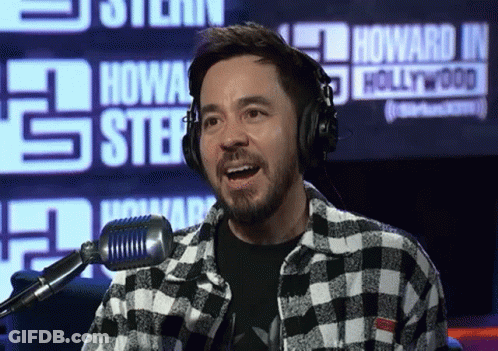 A Man Wearing Headphones Stands In Front Of A Microphone In Front Of A Howard J. Hollywood Sign GIF