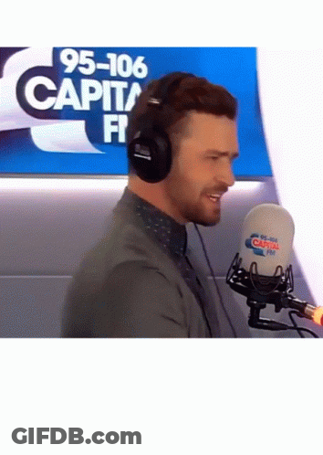 A Man Wearing Headphones Stands In Front Of A Microphone That Says 95-106 Capital Fm On It GIF
