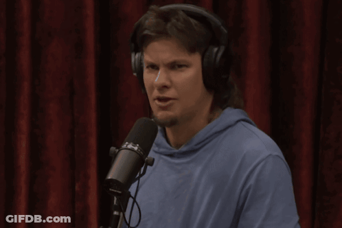 A Man Wearing Headphones Stands In Front Of A Microphone That Says ' Shure ' On It GIF