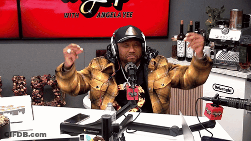 A Man Wearing Headphones Stands In Front Of A Microphone With Angela Yee On The Screen GIF