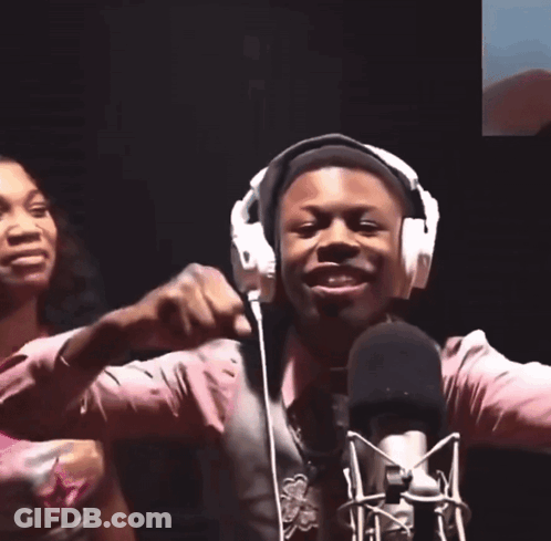 A Man Wearing Headphones Stands In Front Of A Microphone With His Hands In The Air GIF