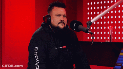 A Man Wearing Headphones Stands In Front Of A Microphone With The Word Snc On His Sleeve GIF