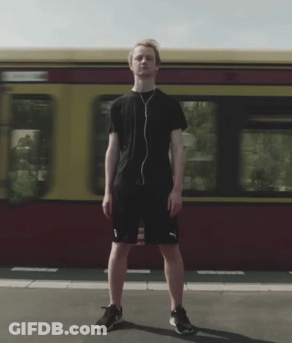 A Man Wearing Headphones Stands In Front Of A Red And Yellow Train GIF