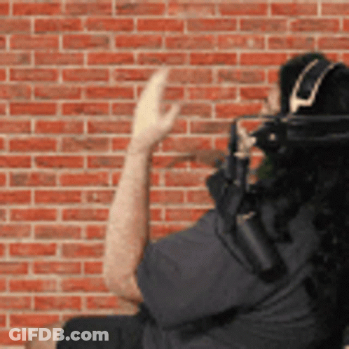 A Man Wearing Headphones Stands In Front Of A Red Brick Wall GIF