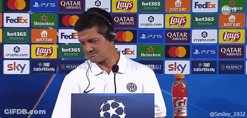 A Man Wearing Headphones Stands In Front Of A Wall Of Advertisements Including Lays And Sky GIF