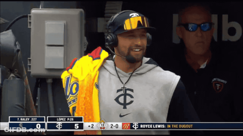 A Man Wearing Headphones Stands In The Dugout With A Scoreboard Behind Him That Says Royce Lewis In The Dugout GIF