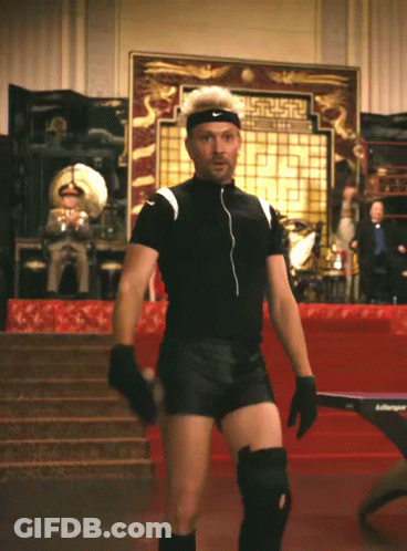 A Man Wearing Knee Pads And A Nike Headband Stands In Front Of A Ping Pong Table GIF