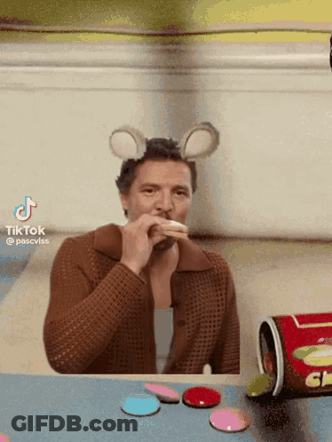A Man Wearing Mouse Ears Is Sitting At A Table With Candy GIF