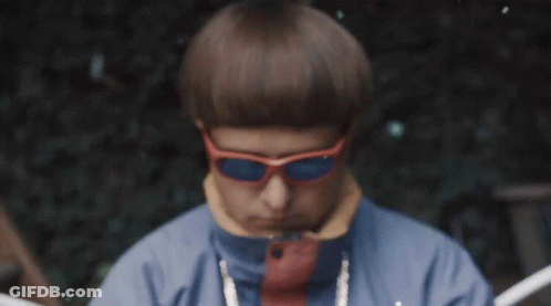 A Man Wearing Orange Sunglasses And A Blue Jacket Looks At The Camera GIF