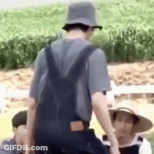 A Man Wearing Overalls And A Hat Is Standing In A Field With A Backpack . GIF