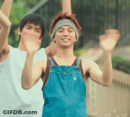 A Man Wearing Overalls And A Headband Is Waving At The Camera GIF