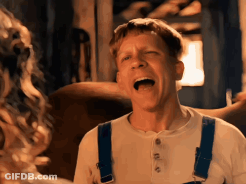A Man Wearing Overalls And A White Shirt Is Making A Funny Face GIF