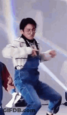 A Man Wearing Overalls And Glasses Is Dancing In A Room . GIF