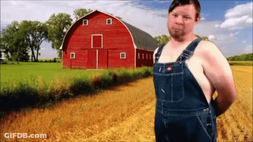 A Man Wearing Overalls Stands In Front Of A Red Barn GIF