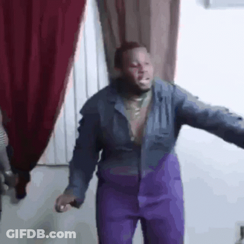 A Man Wearing Purple Pants And A Blue Jacket Is Dancing In A Room . GIF
