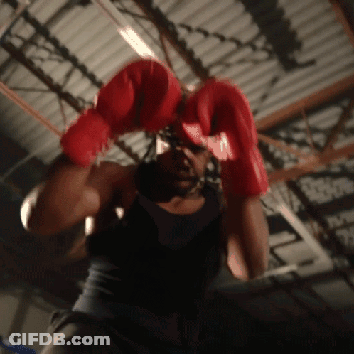 A Man Wearing Red Boxing Gloves Is Hanging From A Ceiling GIF