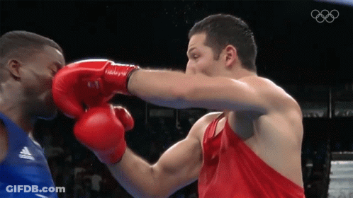 A Man Wearing Red Boxing Gloves Punches Another Man In A Blue Tank Top GIF