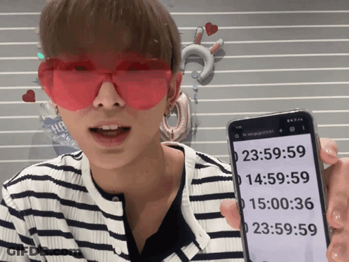 A Man Wearing Red Heart Shaped Sunglasses Is Holding A Cell Phone With The Time 23:59:59 On It GIF