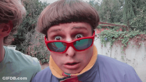 A Man Wearing Red Sunglasses And A Blue Jacket Makes A Surprised Face GIF