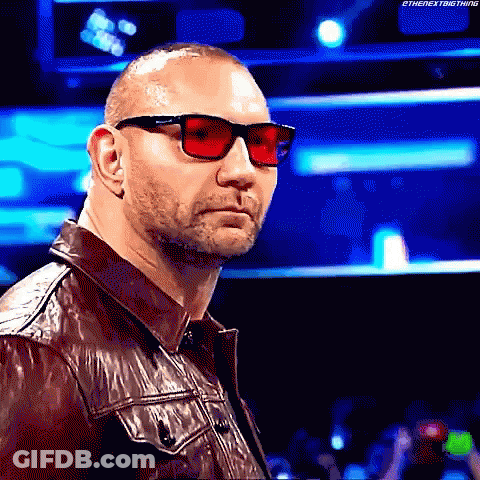 A Man Wearing Red Sunglasses And A Leather Jacket Is Standing In Front Of A Crowd . GIF