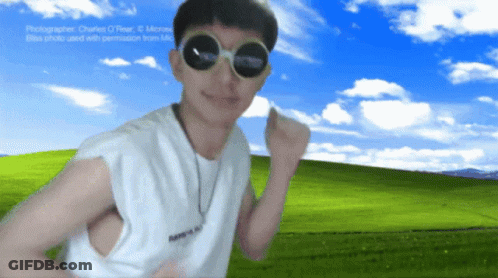 A Man Wearing Round Sunglasses Stands In Front Of A Field GIF