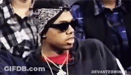 A Man Wearing Sunglasses , A Bandana And A Necklace Is Sitting In A Crowd Of People . GIF