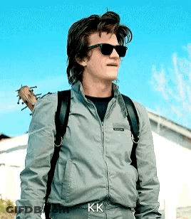 A Man Wearing Sunglasses And A Backpack Is Standing In Front Of A House . GIF
