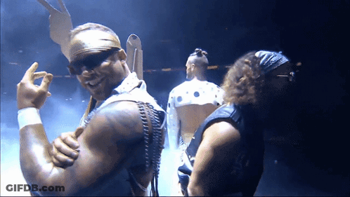 A Man Wearing Sunglasses And A Bandana Stands Next To Another Man In A Dark Room GIF