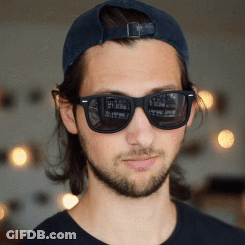 A Man Wearing Sunglasses And A Baseball Cap Has A Reflection Of A Building In His Sunglasses GIF