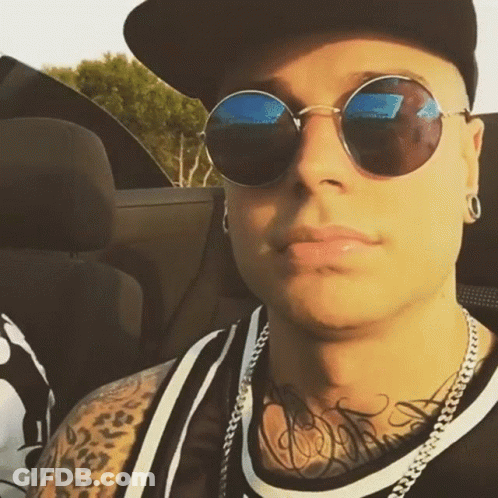 A Man Wearing Sunglasses And A Baseball Cap Is Sitting In A Car GIF
