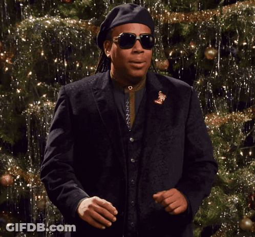 A Man Wearing Sunglasses And A Black Hat Is Dancing In Front Of A Christmas Tree GIF