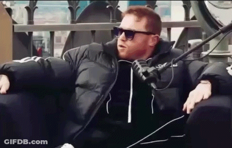 A Man Wearing Sunglasses And A Black Jacket Is Sitting In A Chair With A Microphone . GIF
