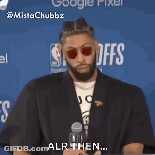 A Man Wearing Sunglasses And A Black Jacket Is Sitting In Front Of A Microphone And Says Alr Then . GIF