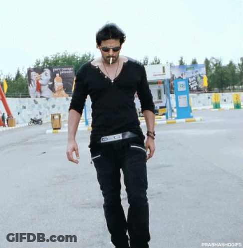 A Man Wearing Sunglasses And A Black Shirt Is Walking Down The Street GIF
