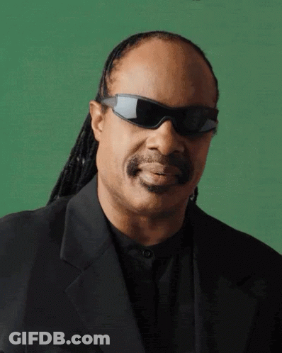 A Man Wearing Sunglasses And A Black Suit Is Smiling GIF