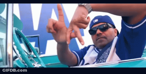 A Man Wearing Sunglasses And A Blue Hat Is Giving The Peace Sign GIF