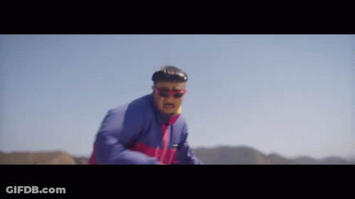 A Man Wearing Sunglasses And A Blue Jacket Is Standing In The Desert GIF