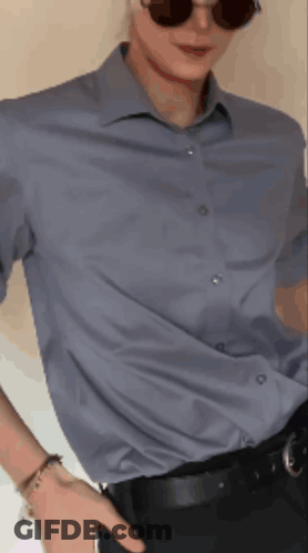 A Man Wearing Sunglasses And A Blue Shirt Holds His Hand In His Pocket GIF