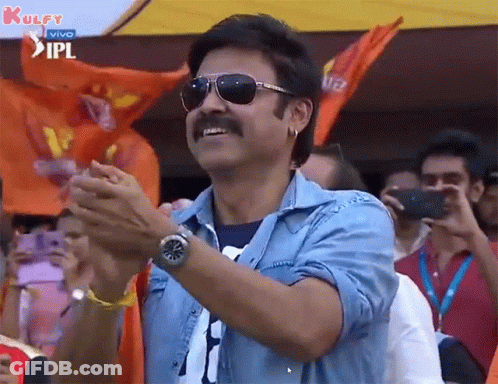 A Man Wearing Sunglasses And A Blue Shirt Is Clapping His Hands In Front Of A Crowd . GIF