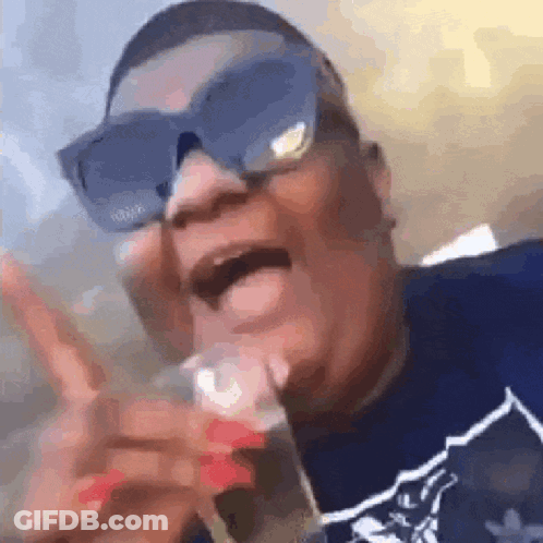 A Man Wearing Sunglasses And A Blue Shirt Is Holding A Glass In His Hand . GIF