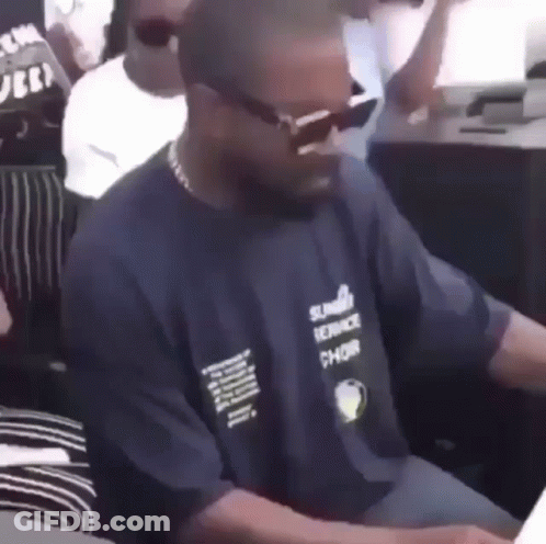 A Man Wearing Sunglasses And A Blue Shirt Is Sitting At A Table In A Crowd . GIF