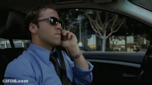 A Man Wearing Sunglasses And A Blue Shirt Is Talking On A Cell Phone GIF
