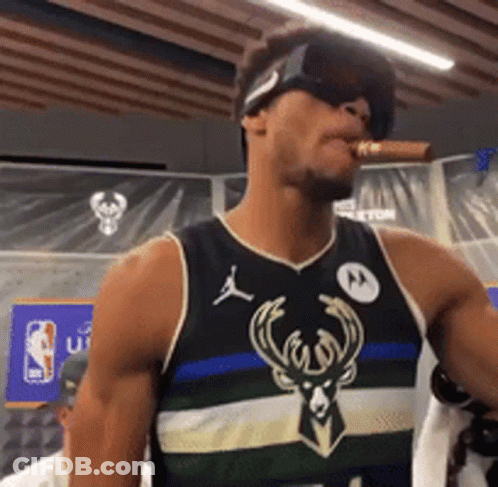 A Man Wearing Sunglasses And A Bucks Jersey Is Smoking A Cigar GIF