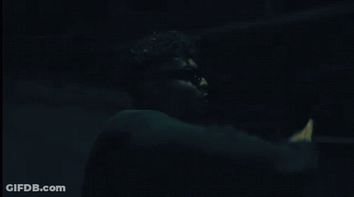 A Man Wearing Sunglasses And A Choker Is Standing In A Dark Room GIF