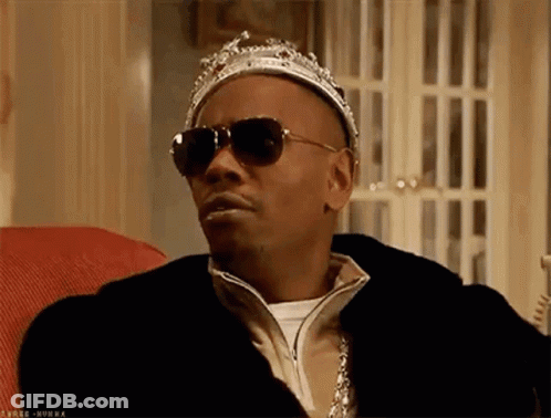 A Man Wearing Sunglasses And A Crown Is Sitting In A Chair . GIF